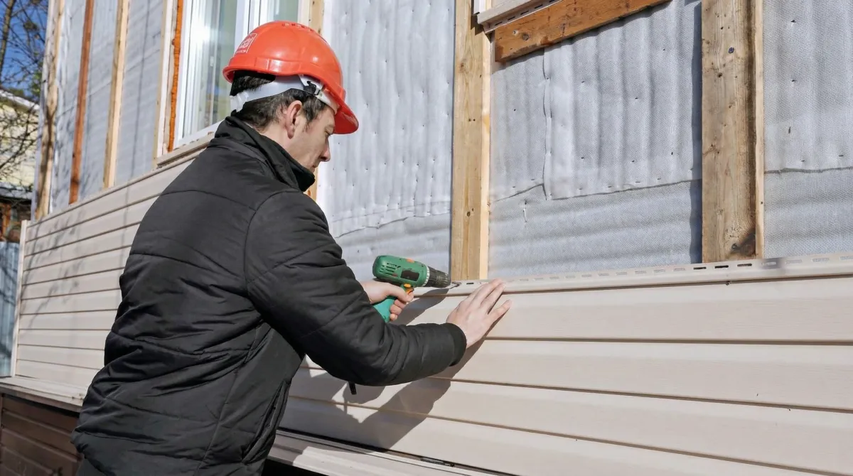 Siding replacement professional using a power drill to install new tan vinyl siding on a home exterior in Columbia, MO